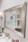 A thick-rimmed. metal mirror displays a renovated shower and bathroom in the image.